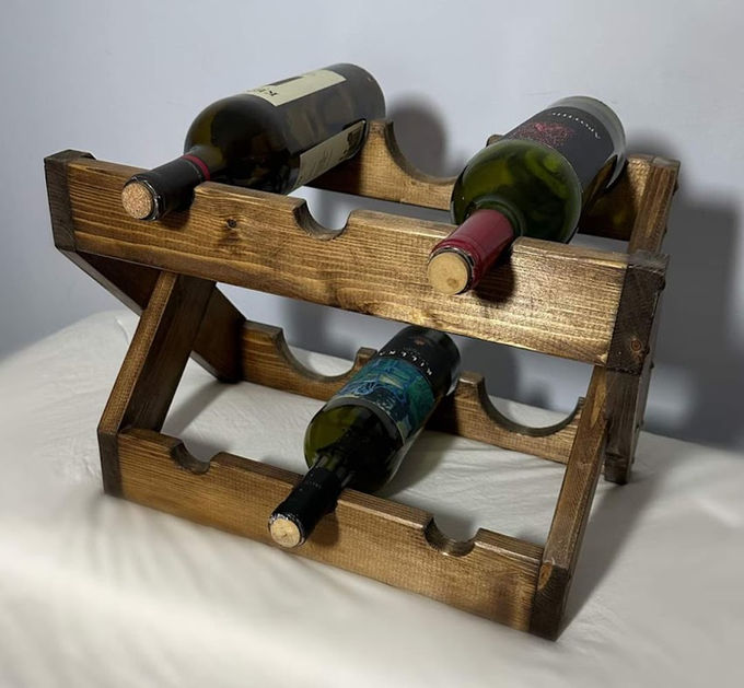 A stained-pine countertop wine rack holding several bottles on stacked angled rails.