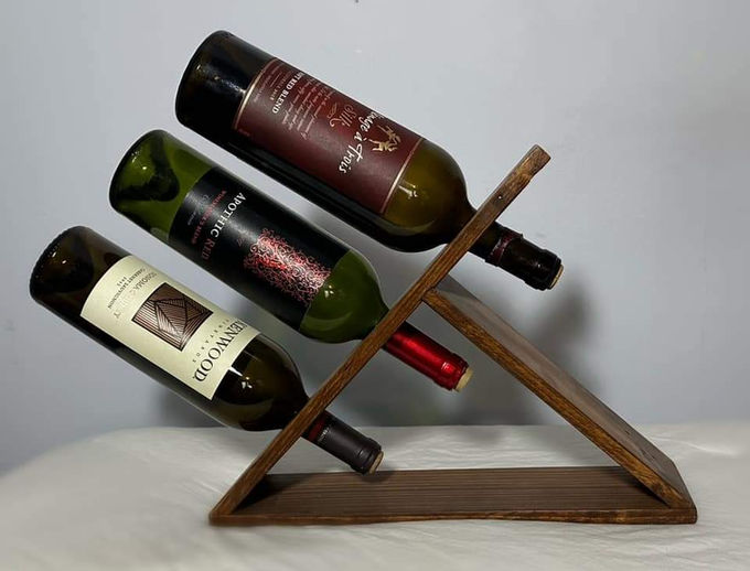 A three-bottle countertop wine rack in walnut-finished pallet wood, holding bottles at a diagonal.
